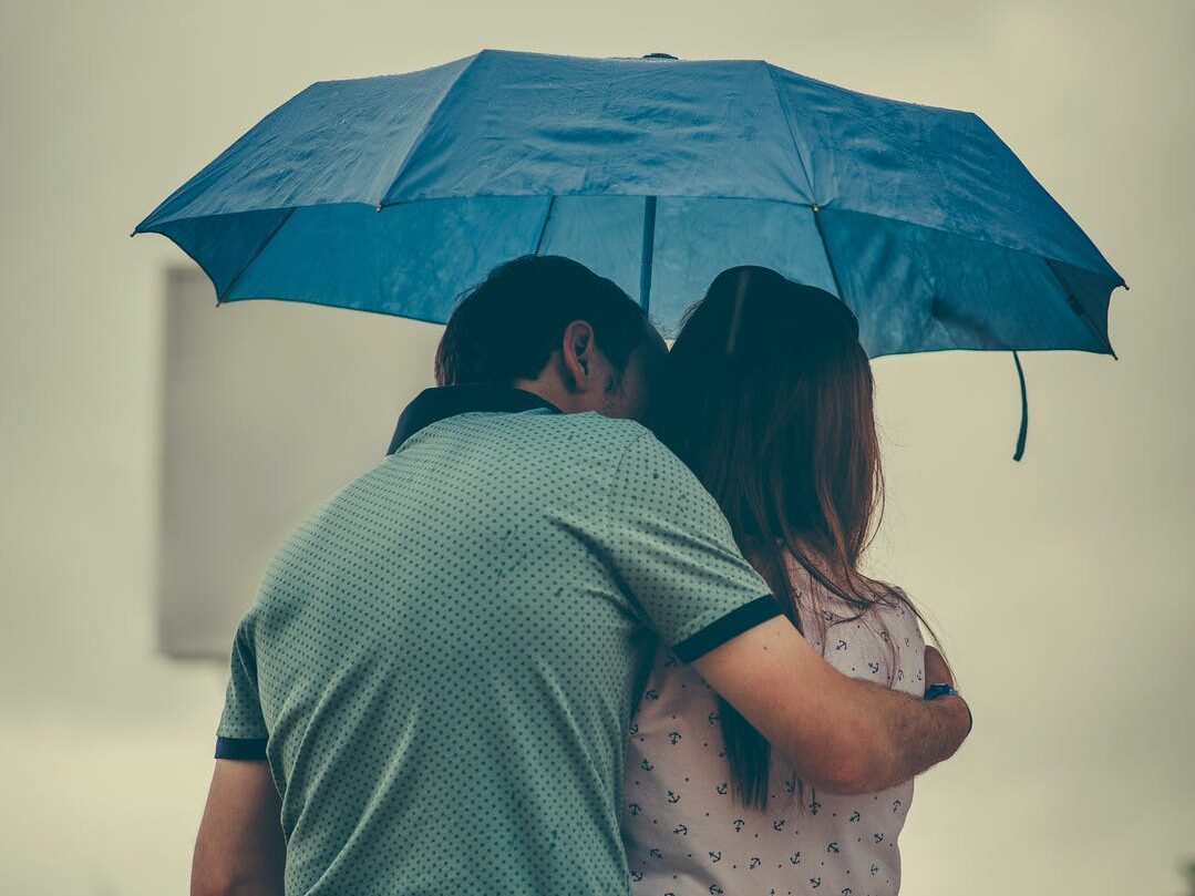 man hugging woman while holding umbrella