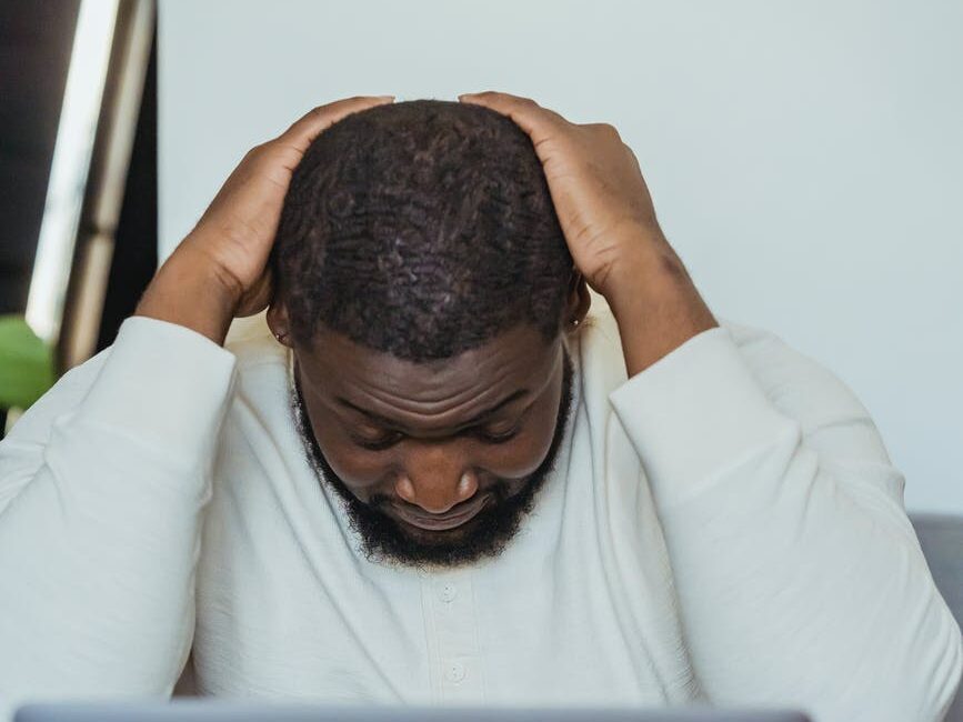 black man lowering head sitting in front of laptop